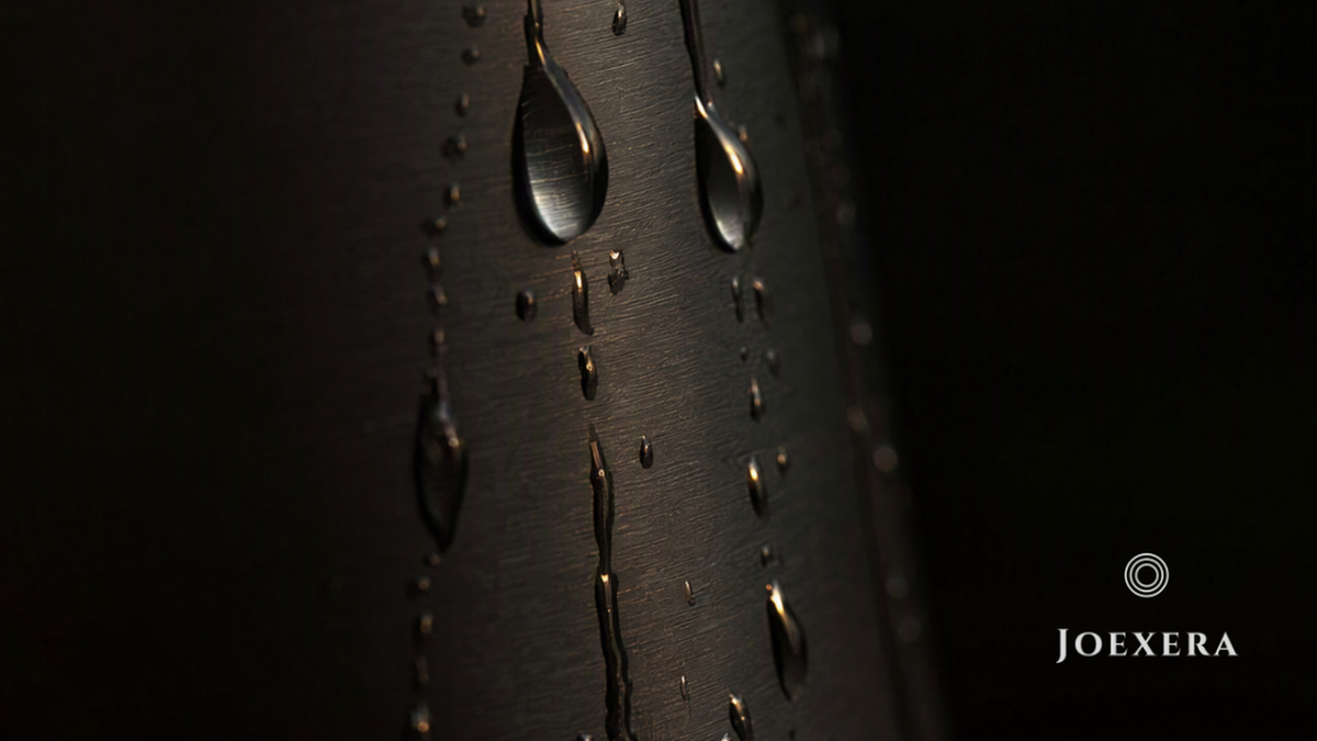 Macro close-up of water droplets on brushed matte black surface — Joexera water wellness